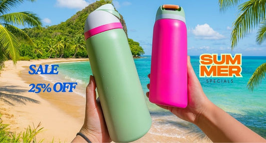 Two hands holding Owala water bottles—one green with a pink band and one hot pink—against a beautiful beach backdrop with turquoise water, white sand, and lush tropical scenery.